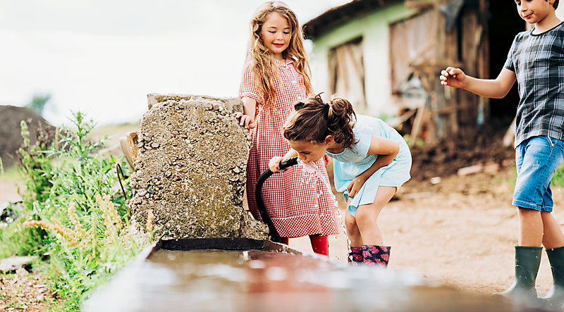 Farmer's children drinking water from a hose.  