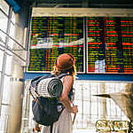 Woman with a backpack and camping equipment looking at the schedules on the scoreboard airport station.