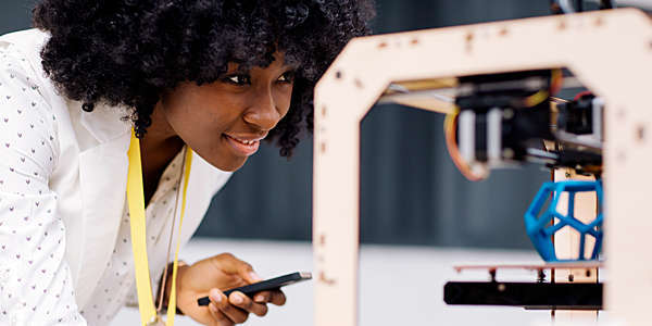 Woman holding her smartphone and printing on a 3D printer.