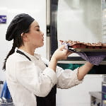 Side view of female chef taking out tray of cookies from oven at commercial kitchen.