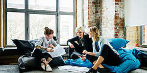 Three businesswomen hold an informal meeting sitting on comfy bean bag cushions at the office.