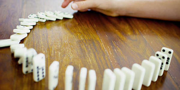 Hand pushing over the first domino of a series to create a chain reaction.