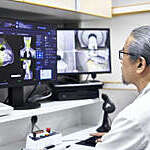 Mature radiologist analyzing MRI scan on computer monitors. Male doctor is sitting at desk in office. He is working at hospital.