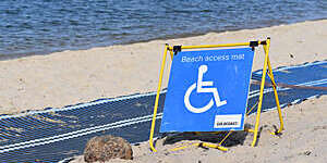 Big blue sign indicating wheelchair access to the beach via a mat rolled out on the sand.