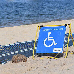 Big blue sign indicating wheelchair access to the beach via a mat rolled out on the sand.