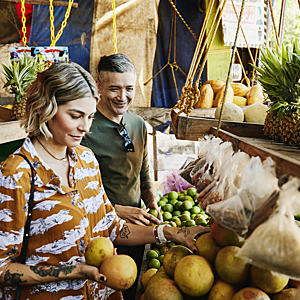 Medium shot of smiling couple picking out fruit at local market while on vacation